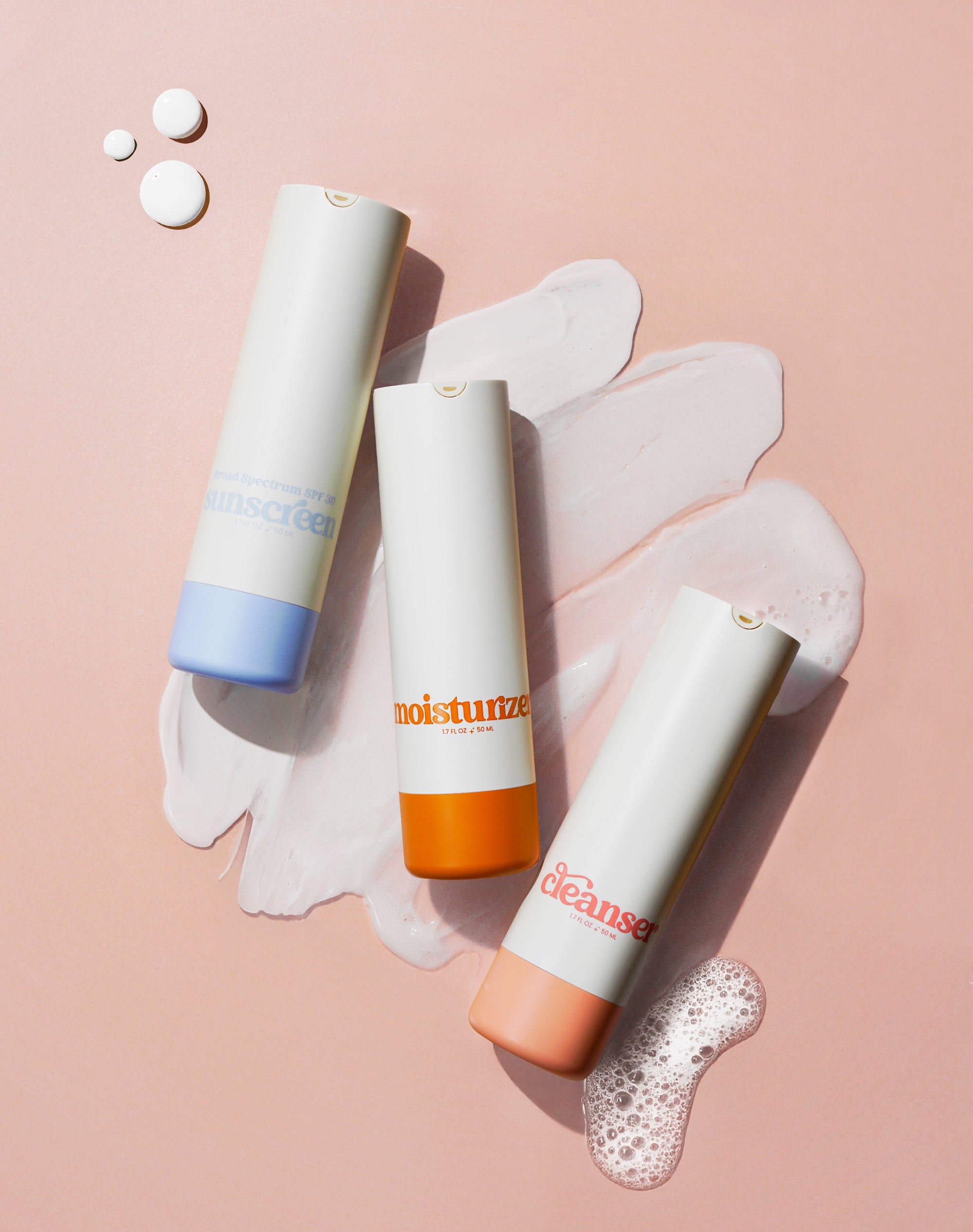 Girlyish cleanser, moisturizer, and sunscreen laying on top of the skincare textures