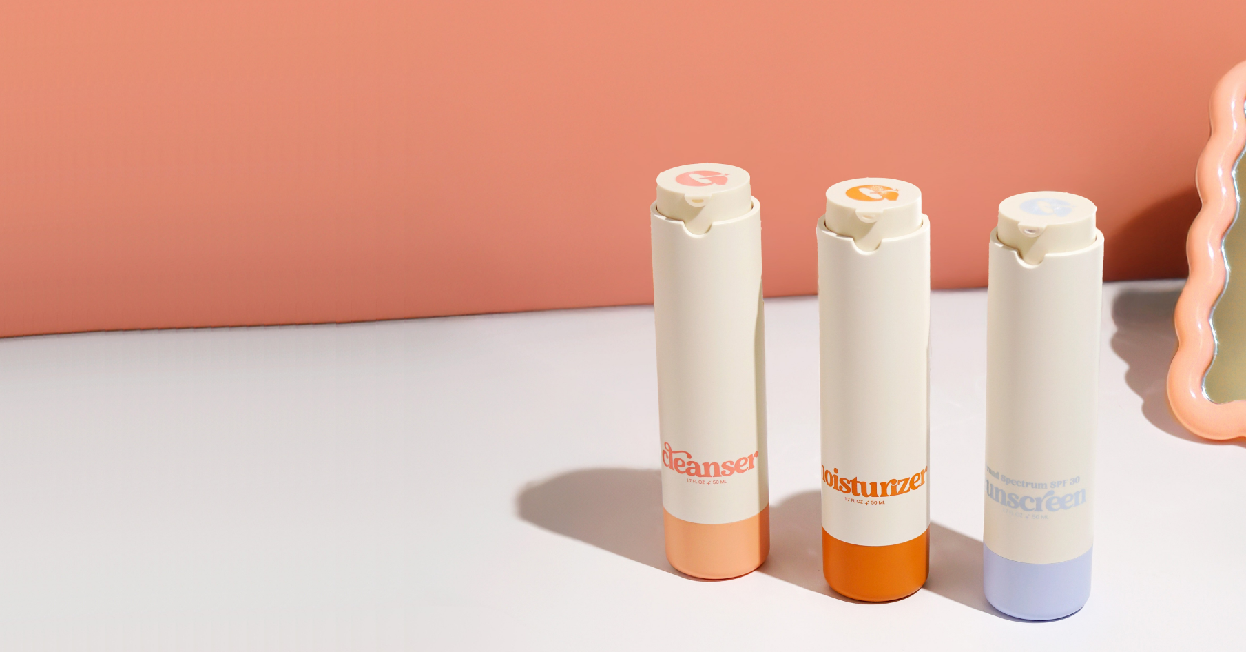 Three minimalist Girlyish skincare bottles labeled cleanser, moisturizer, and sunscreen, standing in a row on a peach and white background.