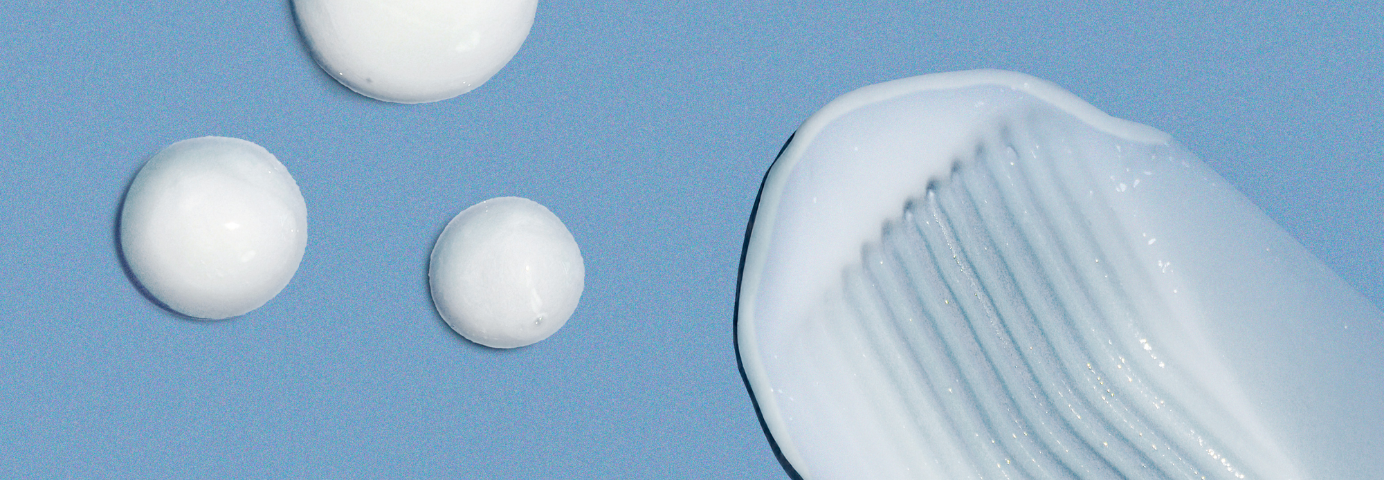 A close-up of white skincare cream textures on a blue background. The image includes three round blobs and one larger swipe pattern, showcasing the product's consistency and smoothness.