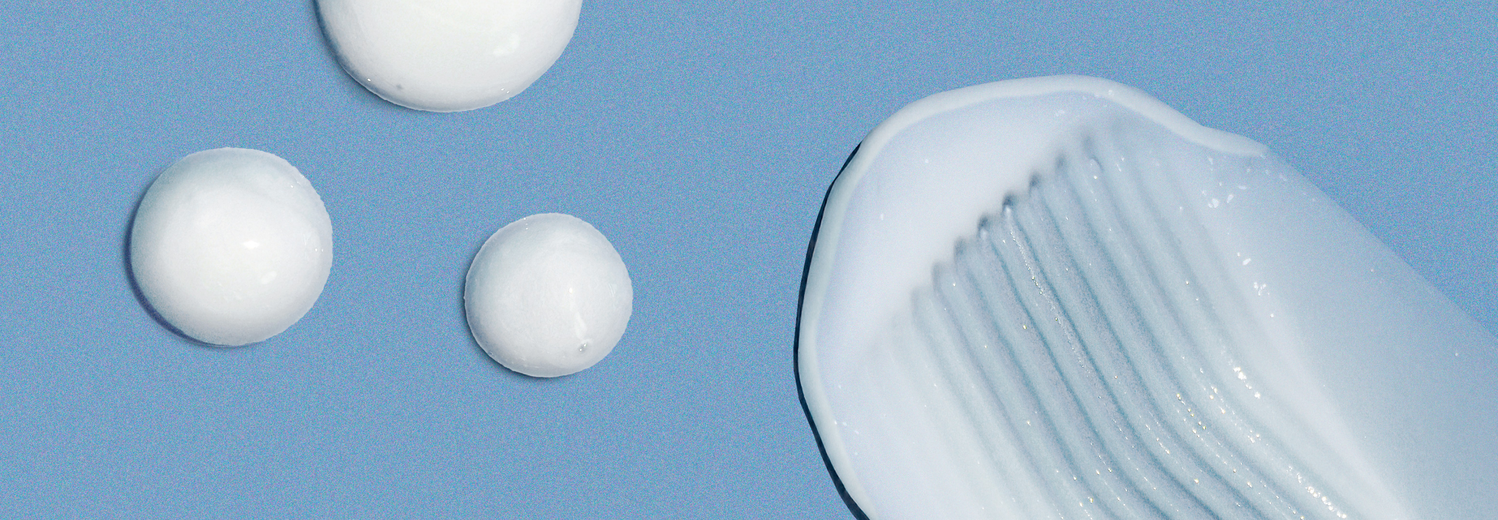 A close-up of white skincare cream textures on a blue background. The image includes three round blobs and one larger swipe pattern, showcasing the product's consistency and smoothness.