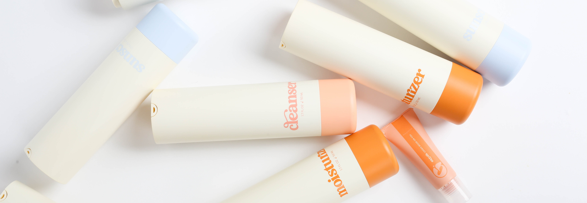 A flat lay image of Girlyish skincare bottles, including labeled products like cleanser, moisturizer, and sunscreen. The bottles are arranged diagonally on a white background, with soft, pastel-toned packaging.