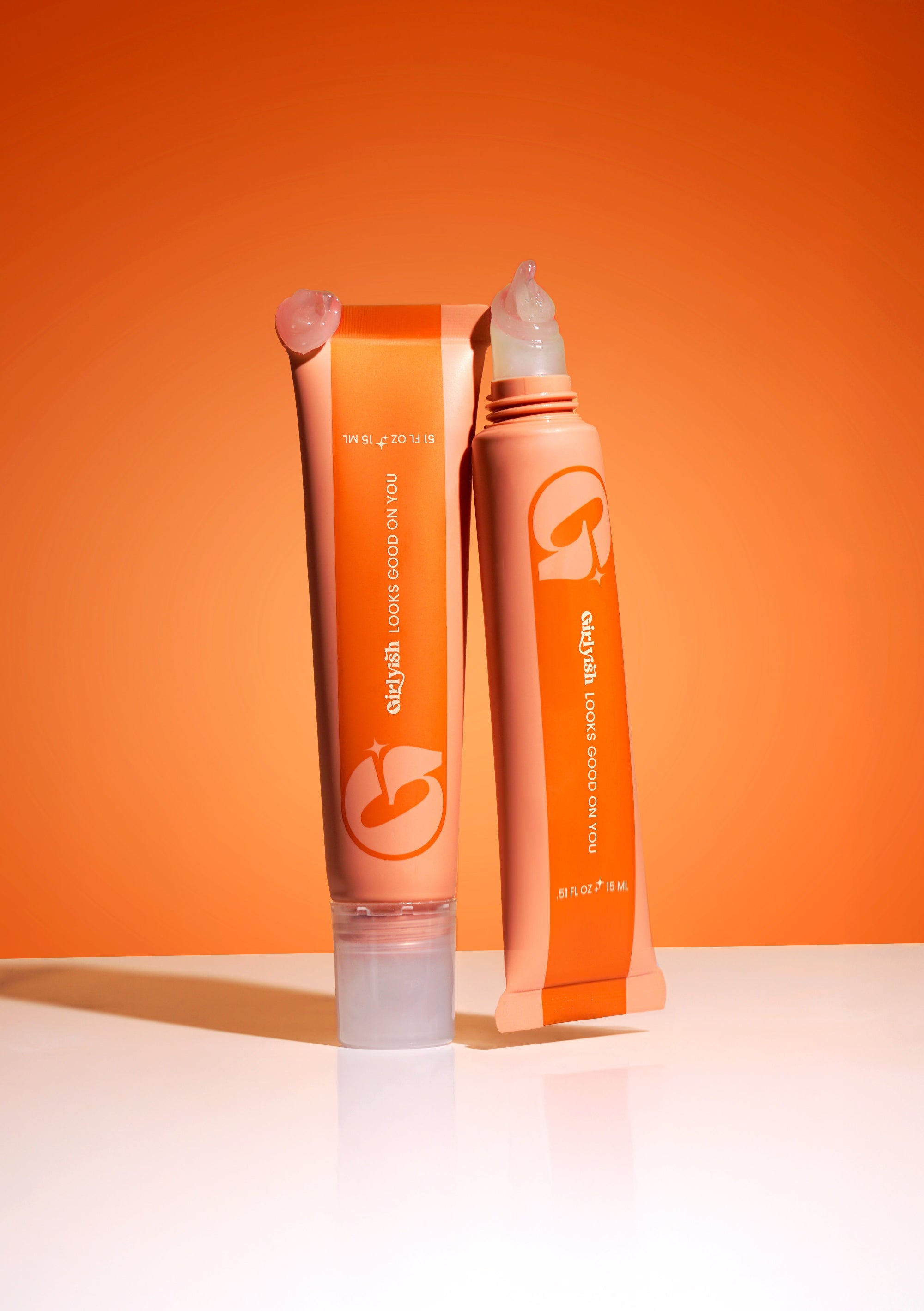 Two girlyish skincare lip balms in front of an orange background